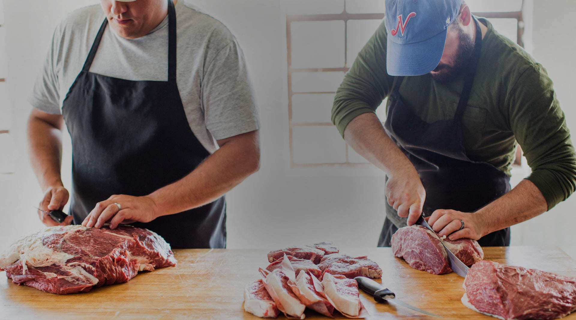 Two Porter Road butchers cutting beef primals into steaks at a wooden butcher block