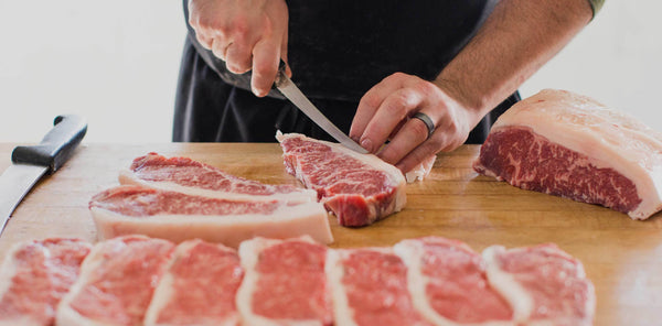 Butcher hand-cutting New York Strip steaks