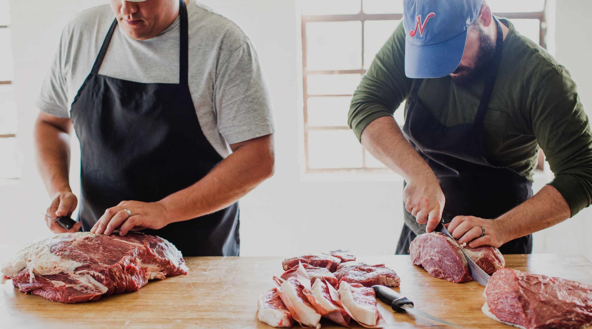 Two butchers hand-cutting beef steaks on a wooden butcher block